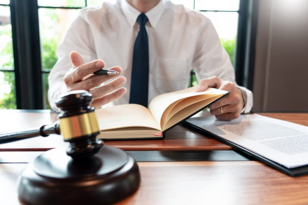 man wearing shirt and tie sits behind desk writing in notebook with gavel in front of him