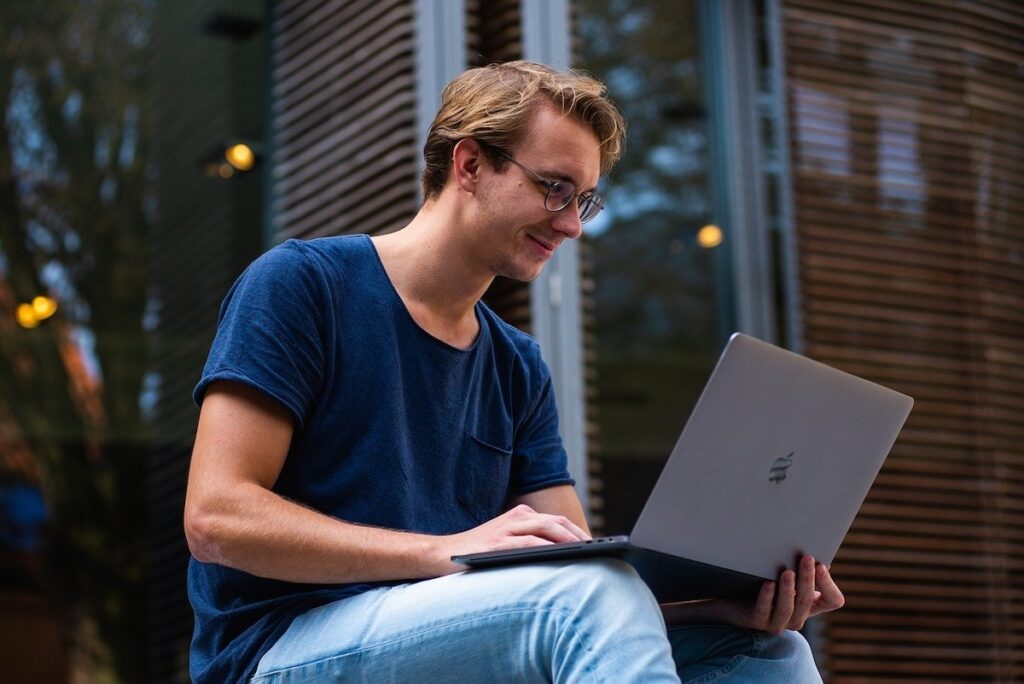 young man sits outside working on laptop