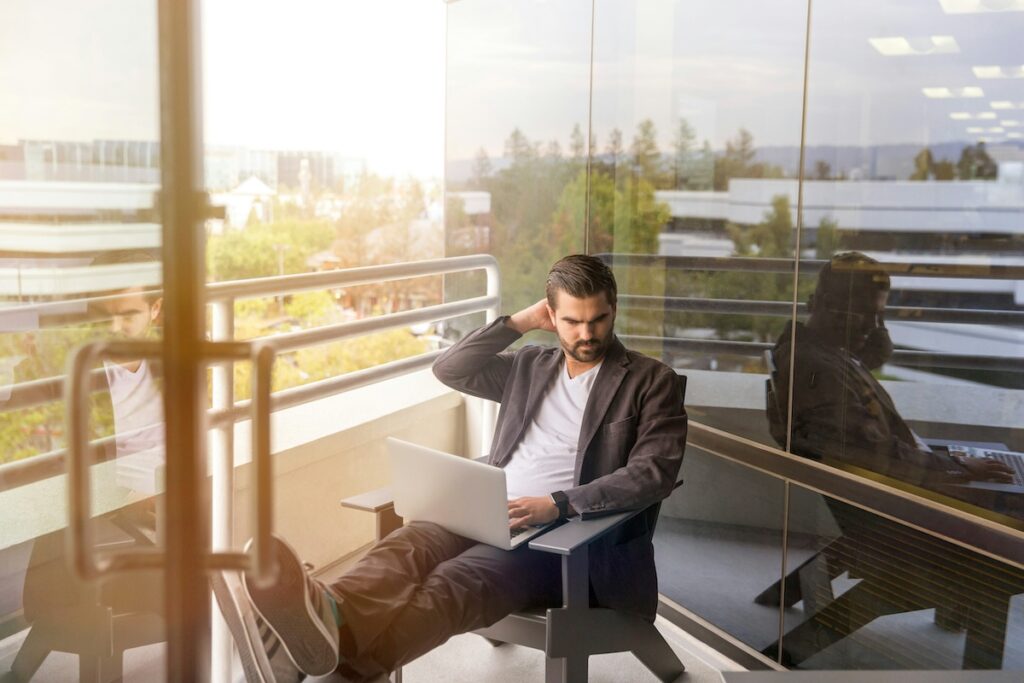 man in suit working on laptop while sitting on balcony