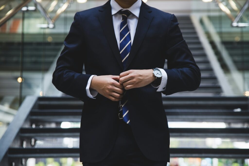 man buttoning suit with sleek business building in background