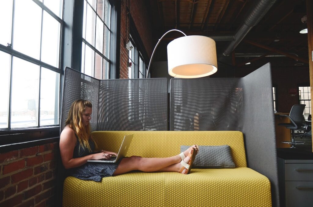 student sits on yellow couch studying on laptop