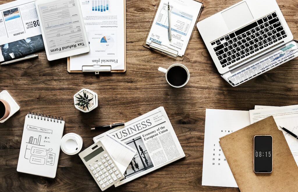 flatlay of a desk with a laptop, notepads, and business pages