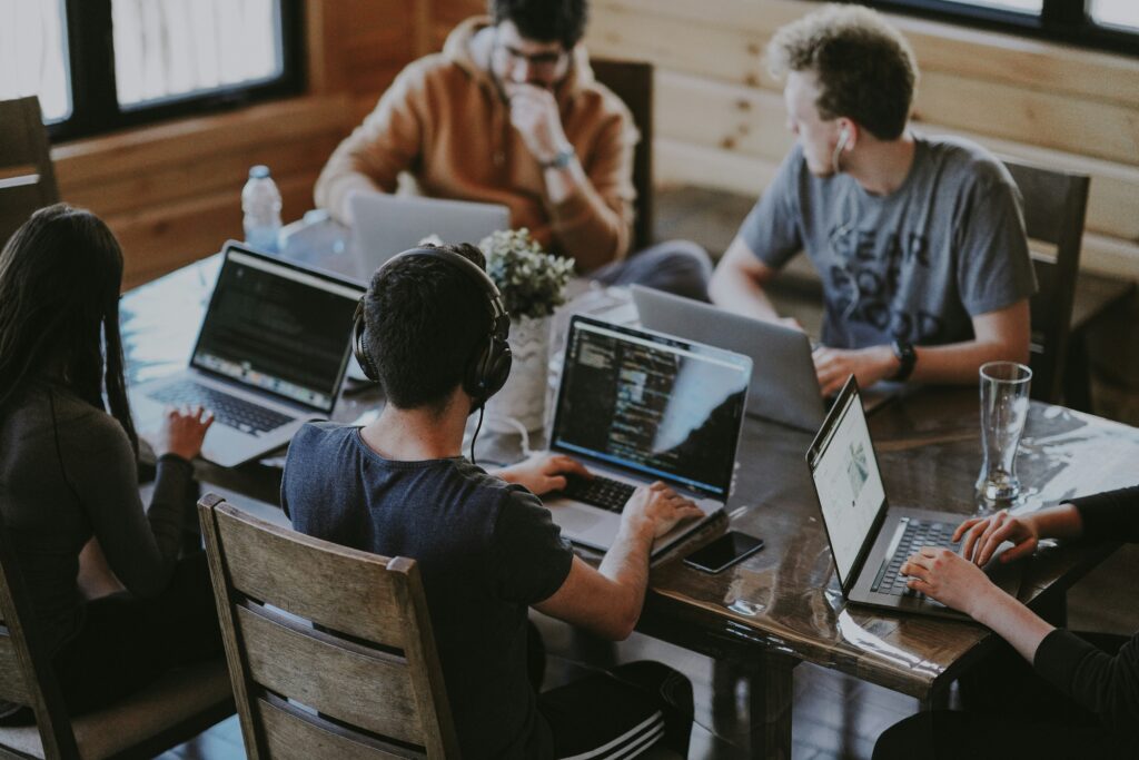 students talk while sitting together at a table with laptops