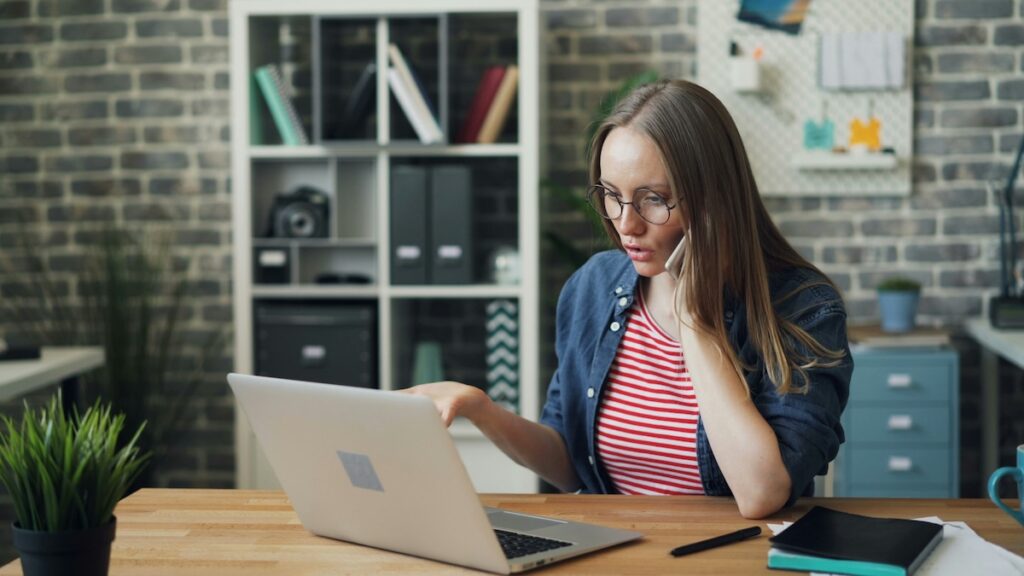 female student talks on phone while working on laptop