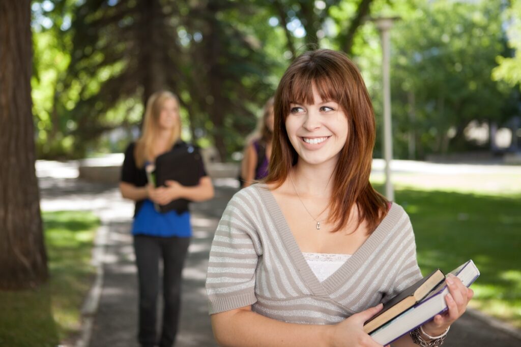 female brunette university student carries books in her left arm