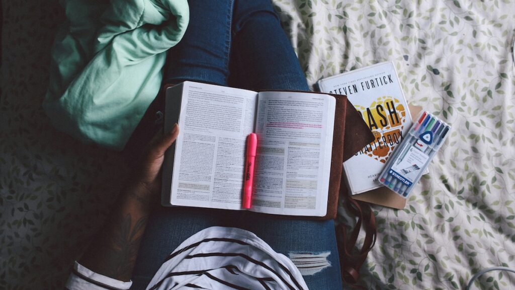student sits on bed with study materials in their lap