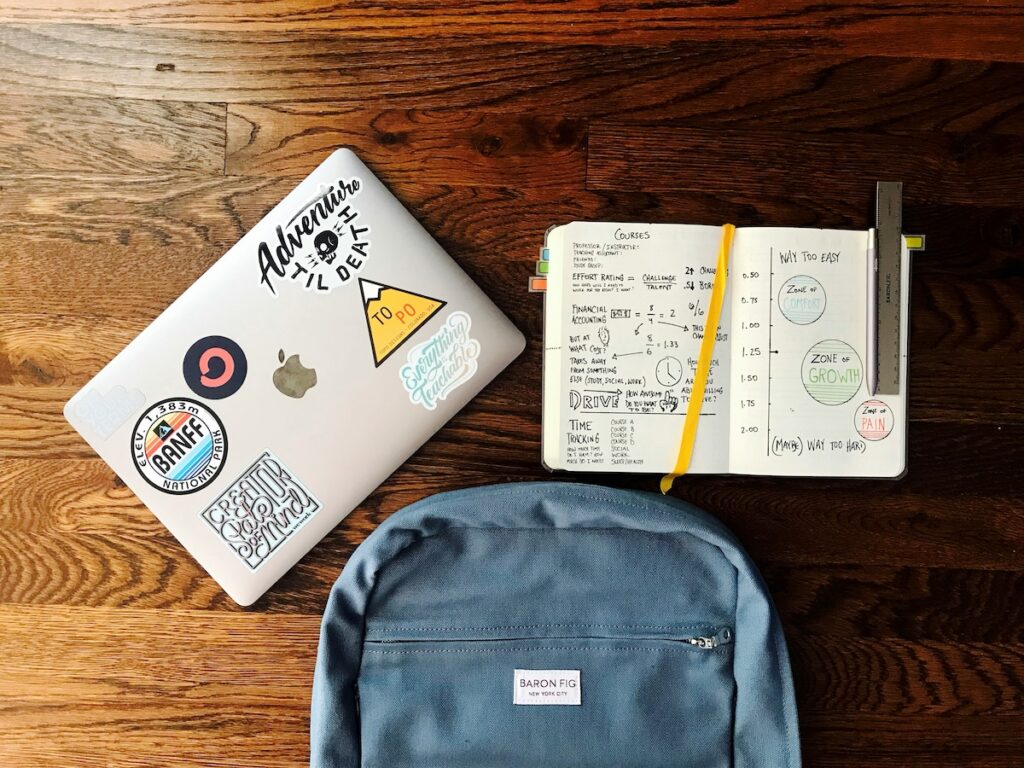 flatlay image of a backpack, laptop and open notebook on a desk