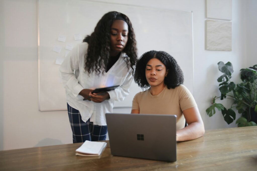 woman works at laptop while another woman looks over her shoulder