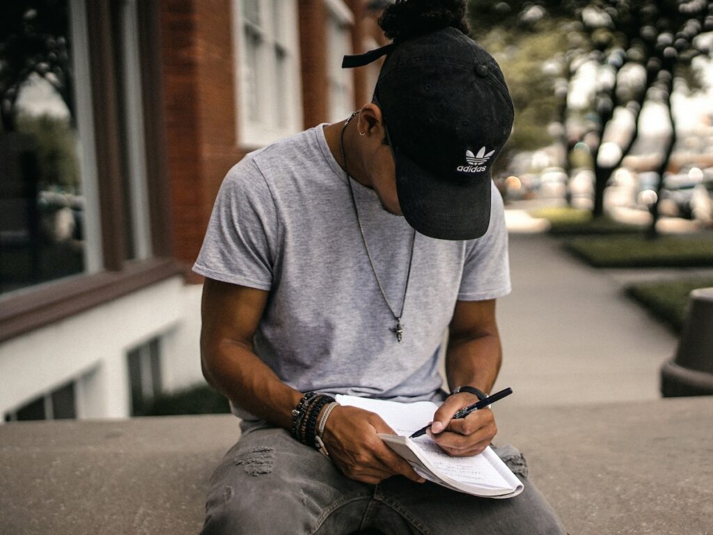 man writing in a journal while sitting outside