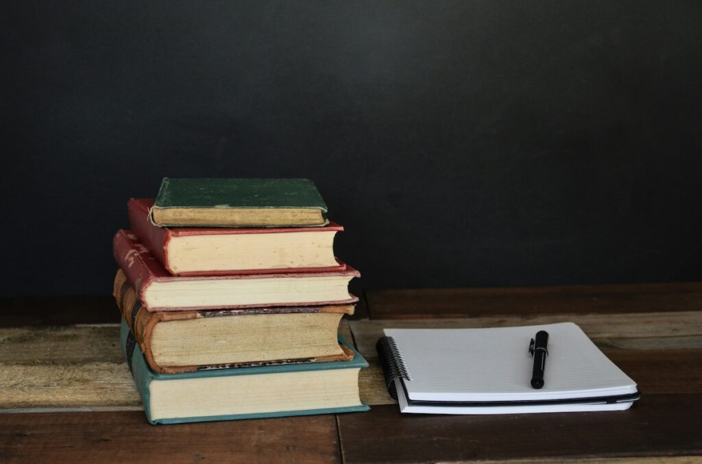 stack of books next to an open notebook on a wooden desk