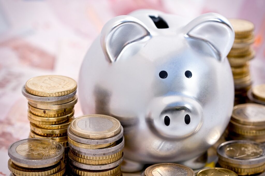 silver piggy bank surrounded by stacks of coins