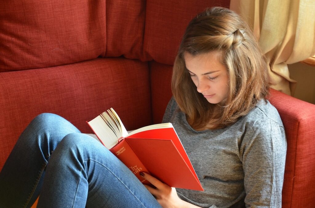 female student sits on red couch reading a book