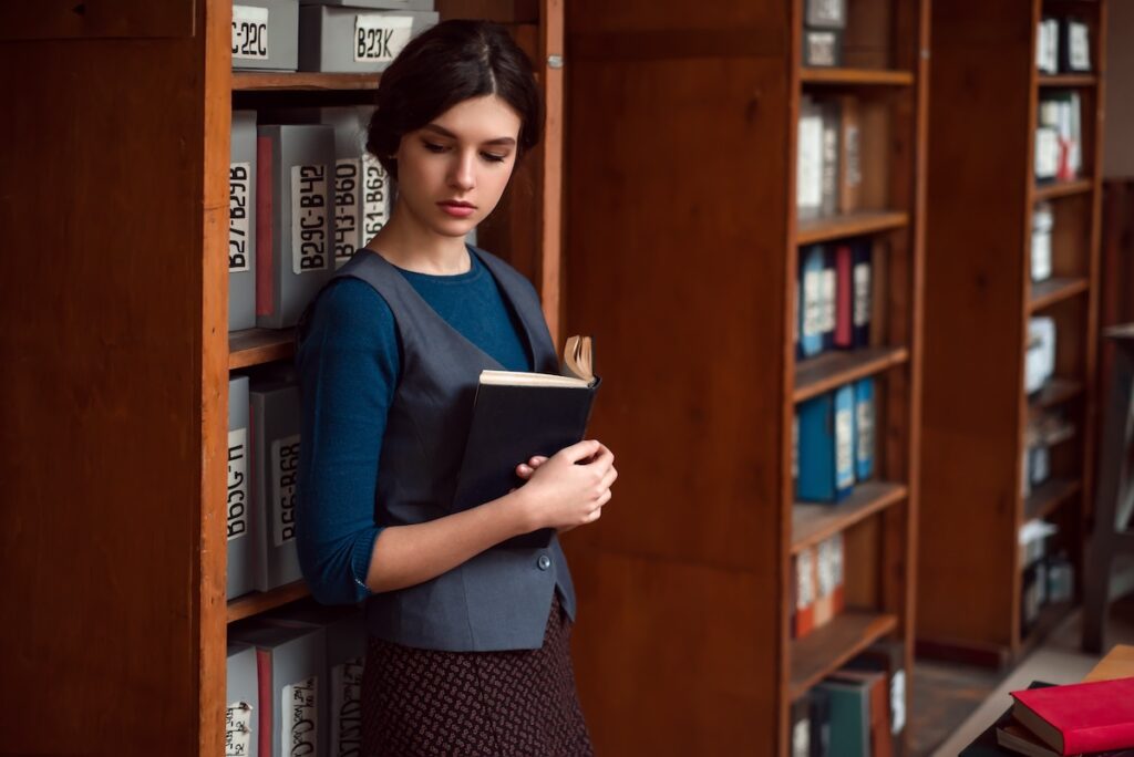Young woman with book in hands standing between bookshelves at the school law library.