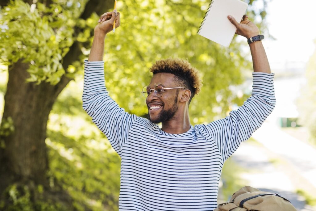 excited student smiles with hands raised over his head