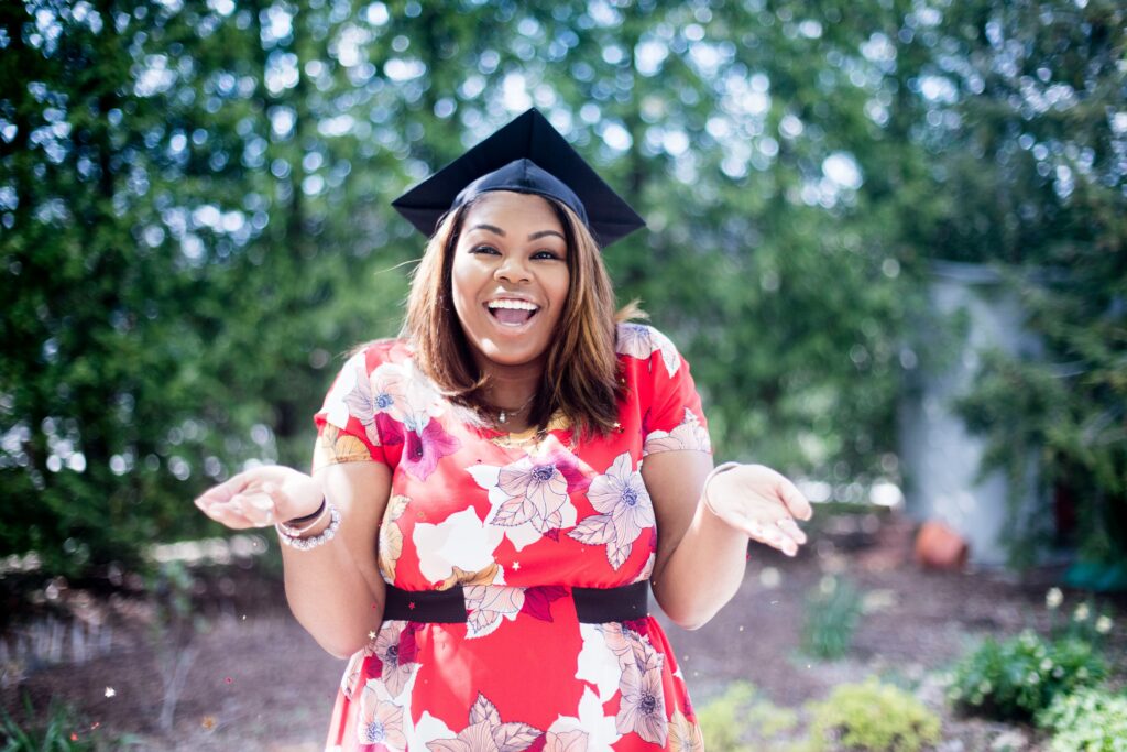 an excited woman wearing a red and white dress and graduation cap smiles at the camera