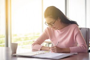 Graduate applicant narrowing a list of grad schools to apply to at a sunlit kitchen table