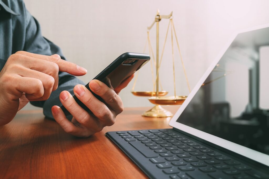 Male lawyer in office with the balance brass scale,hand working with smart phone and digital tablet computer on wooden desk