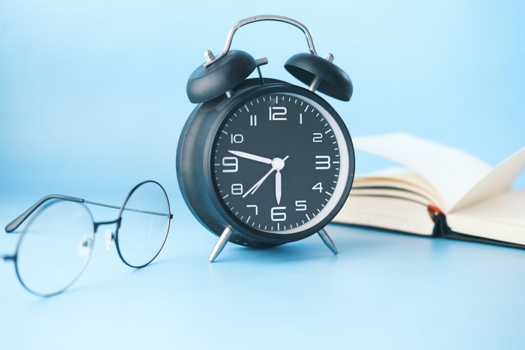 alarm clock next to notebook and glasses