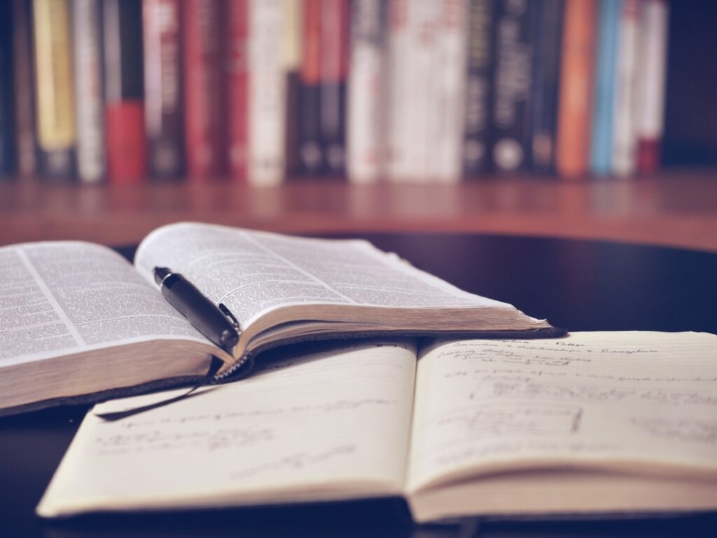 open book and open notebook lay on desktop with bookshelf in the background
