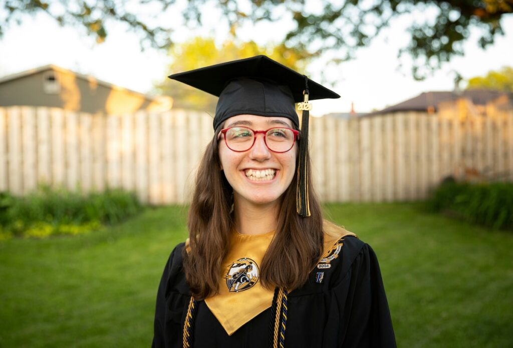beaming graduate stands in graduation robes and cap