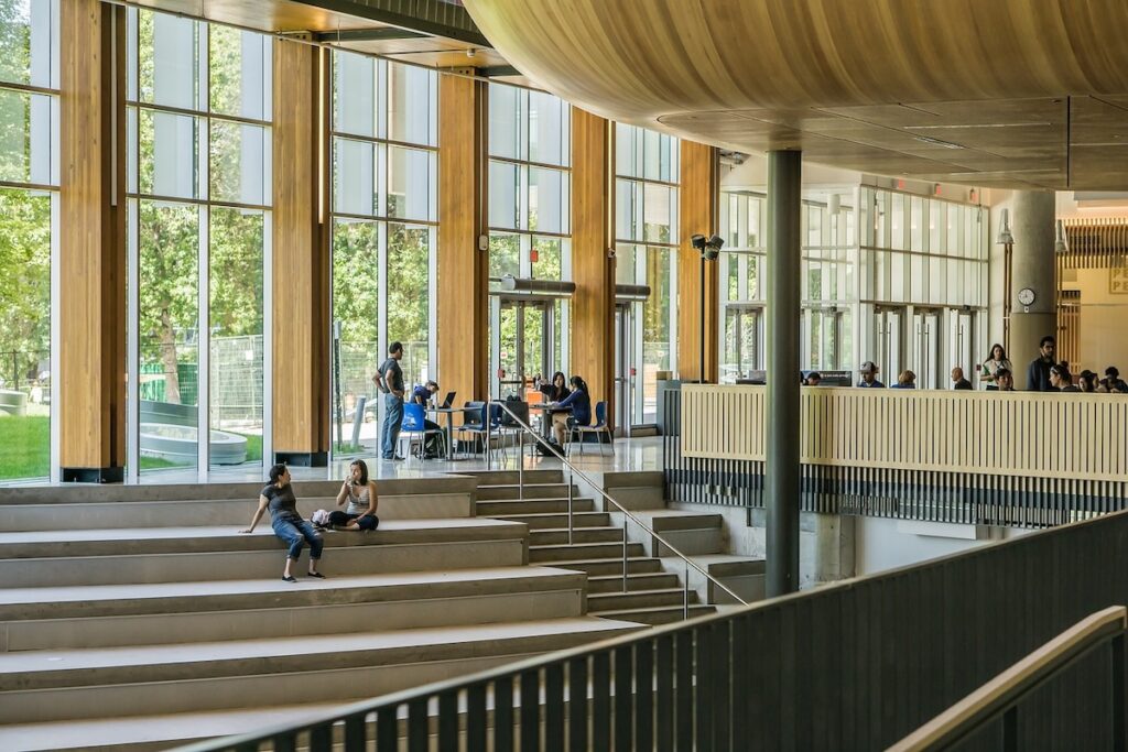 students sit on indoor staircase of university foyer