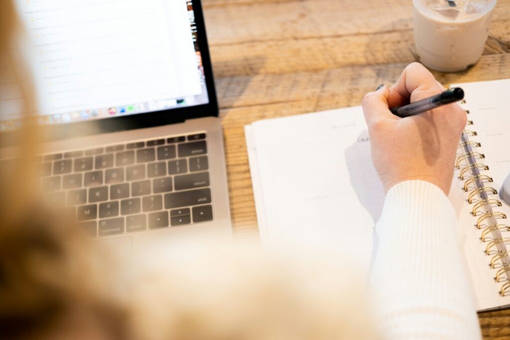 woman writes on notebook next to her laptop