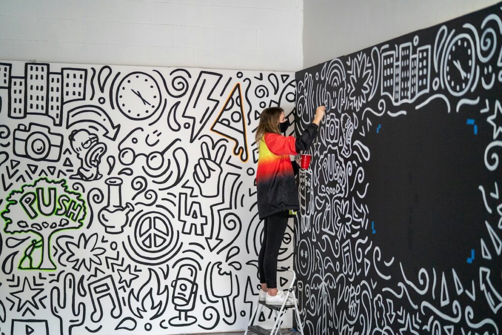 student paints a mural while standing on a ladder