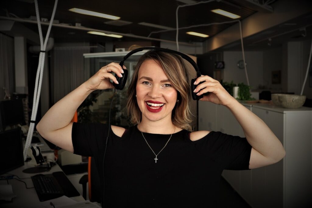 smiling woman places headphones over her ears in recording studio