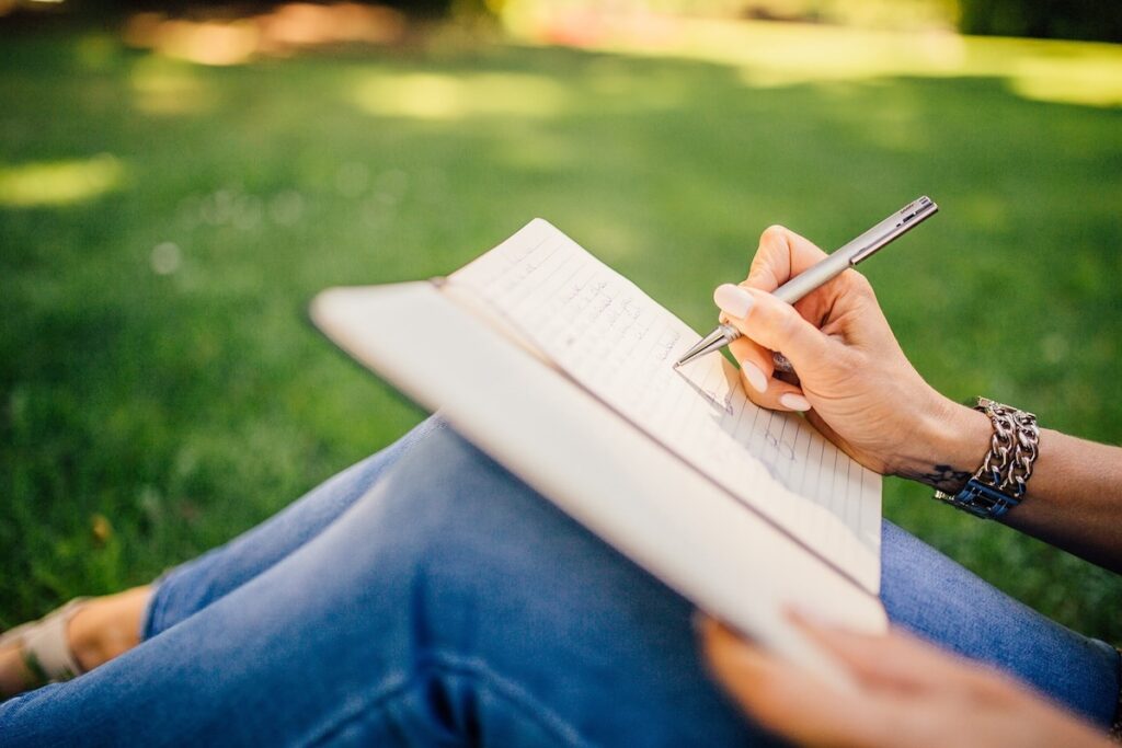 young woman sits outdoors writing in a notebook