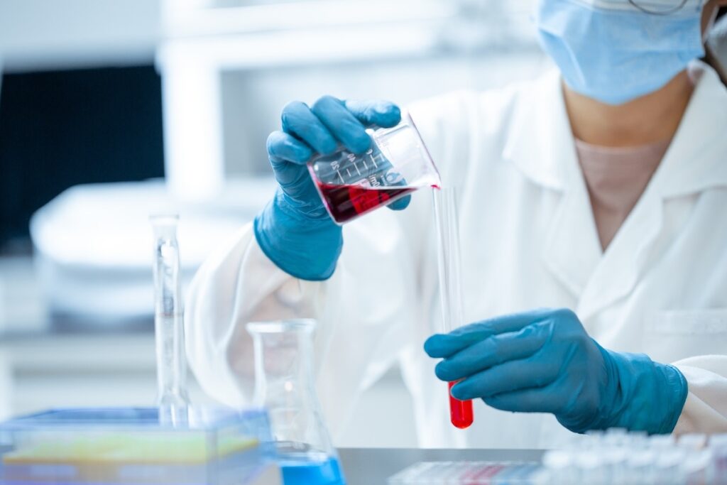 doctor pours red liquid from beaker into test tube in lab environment