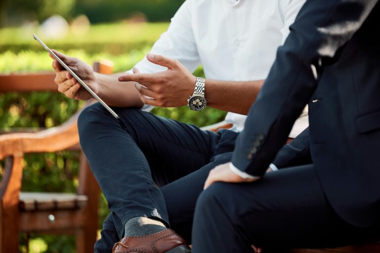 two men on a bench in business attire reviewing document on ipad