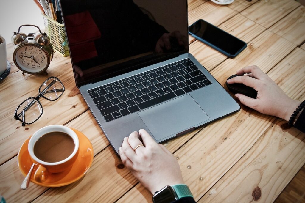 close up of person typing on laptop at a wooden desktop with an orange mug of coffee next to them