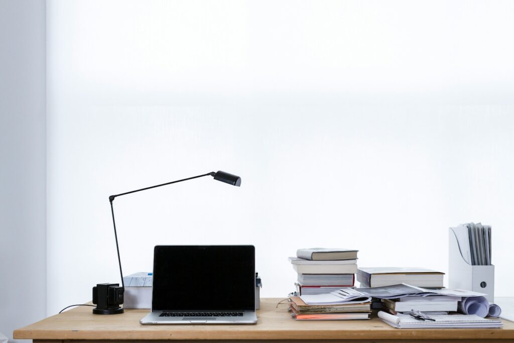 desk with laptop and stacks of books and notebooks