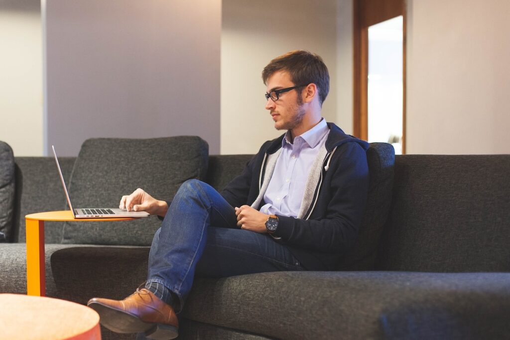 man sits on couch working on laptop in an office environment