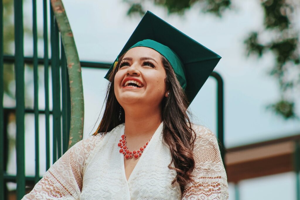 female student smiles with joy while looking toward the sky wearing graduation cap