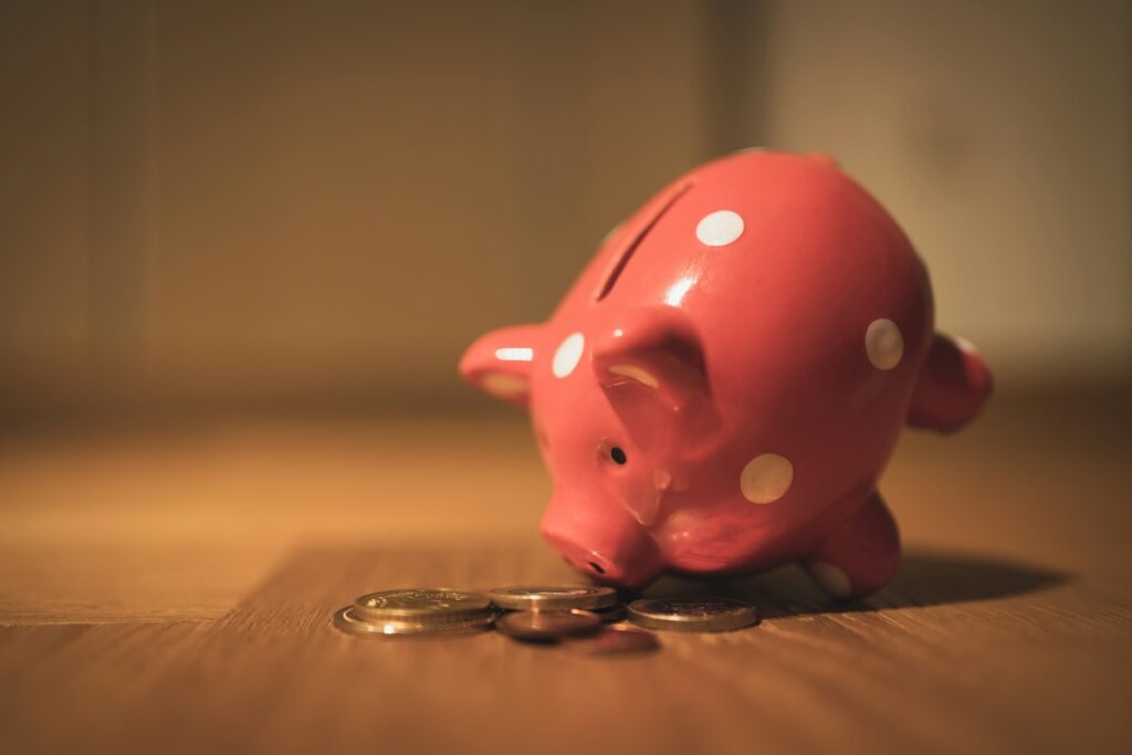 piggy bank tipped forward on wooden desk with coins in front of it