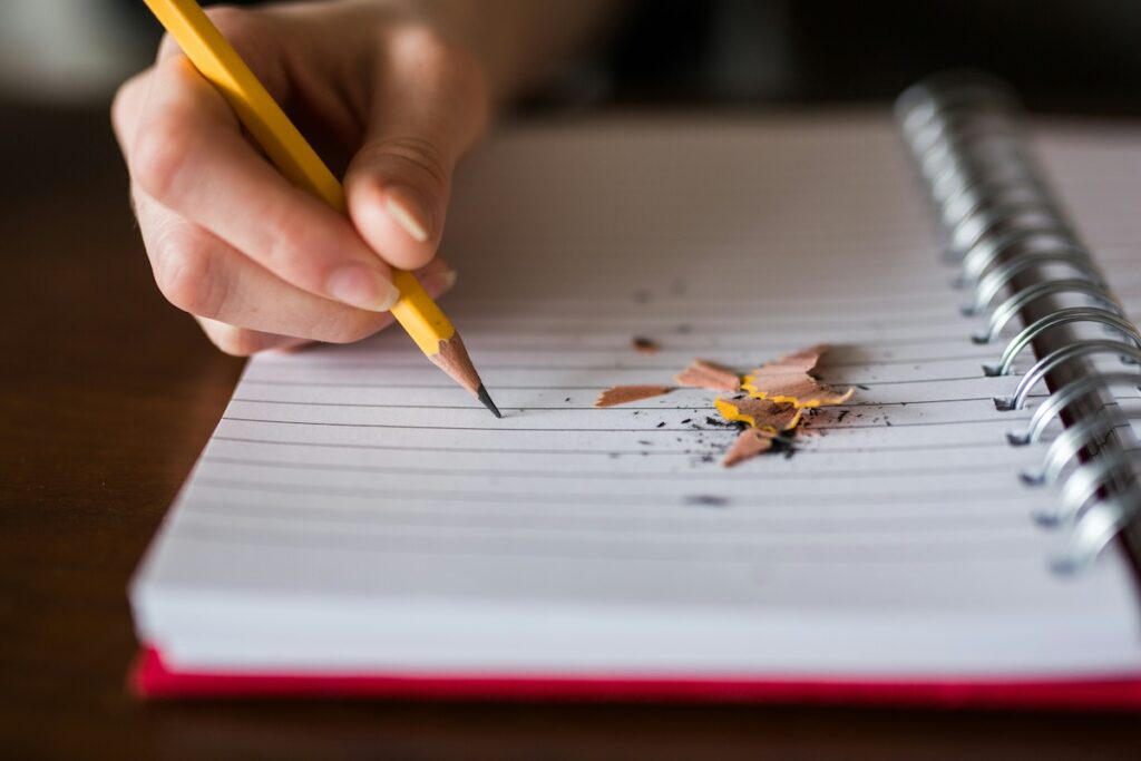 hand writing in notebook with pencil and pencil shavings on the page