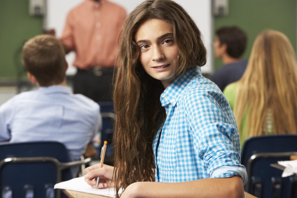 female student with long brown hair and a blue shirt in a classroom with other students