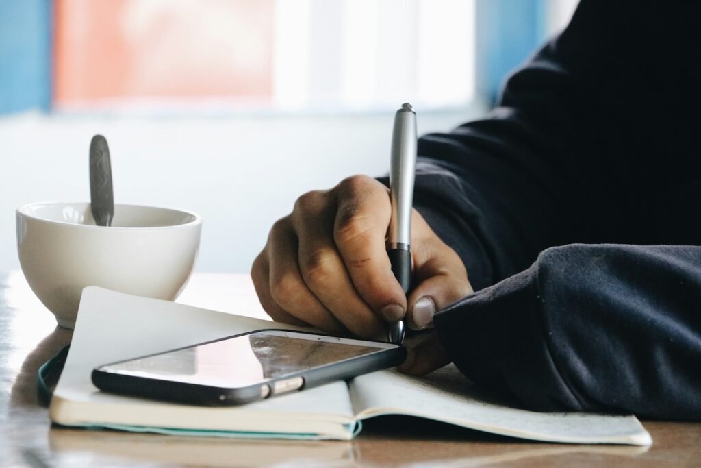 student writes in notebook with smartphone sitting on top of the page