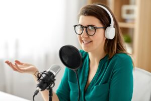 woman in glasses with microphone and headphones talking and recording podcast at studio