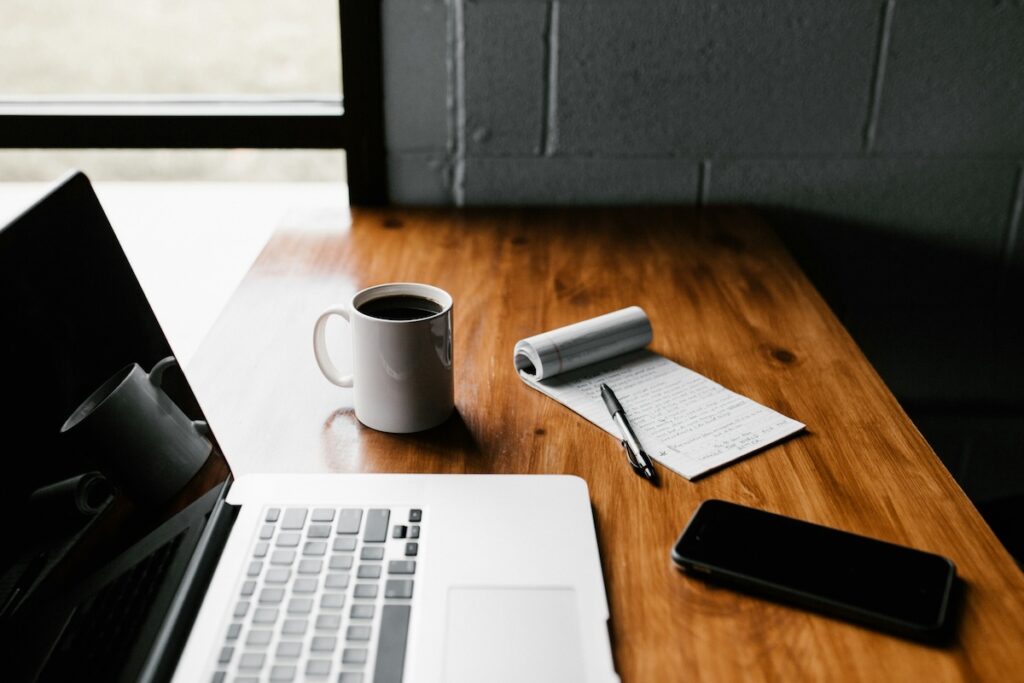 wooden desk with laptop, coffee cup and notepad on top