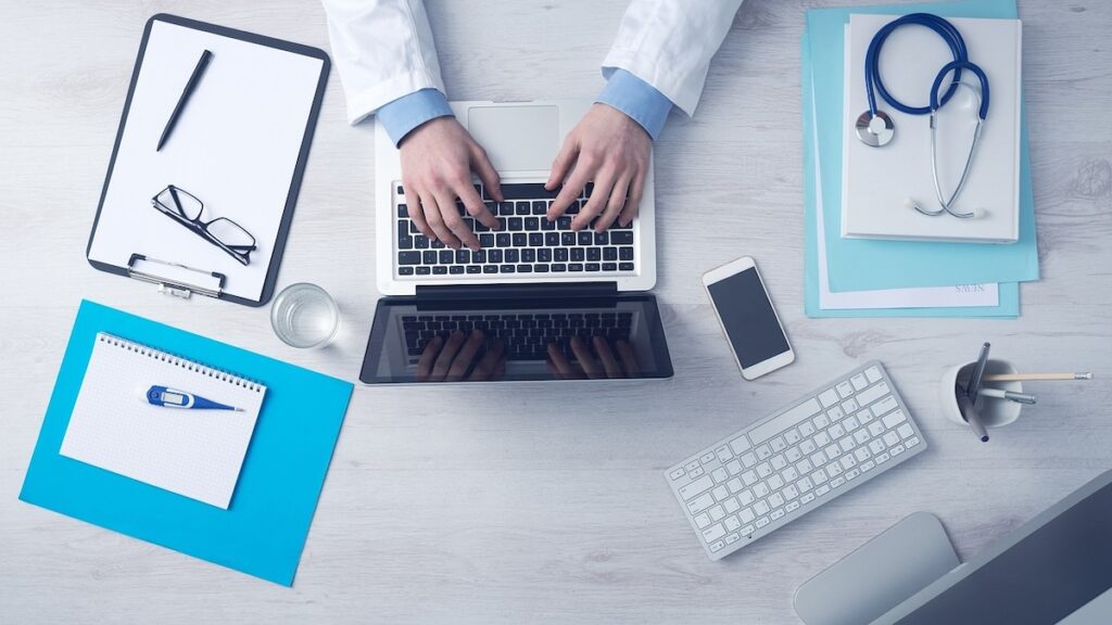 flatlay of desk with stethoscope, laptop, notepad