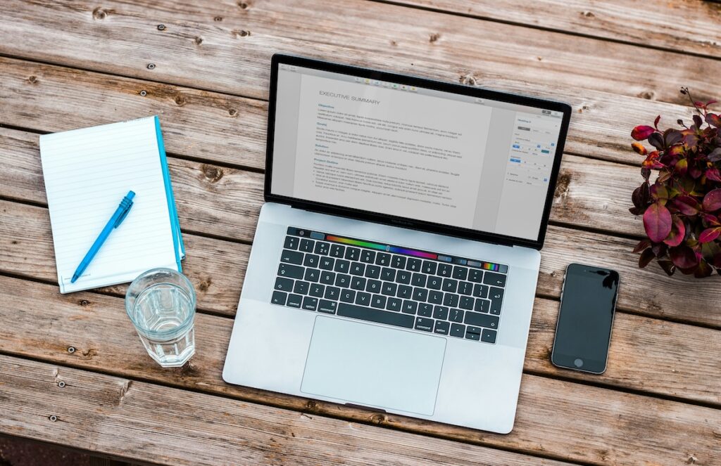 laptop on a table with notepad, phone and glass of water
