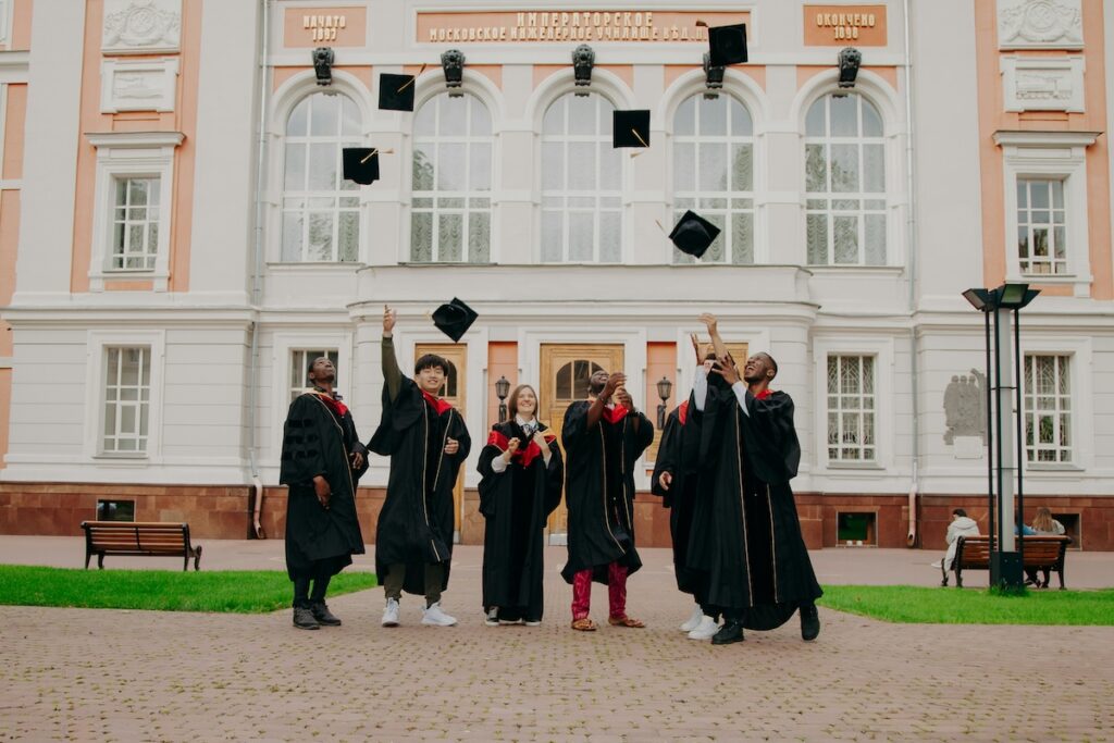 group of graduates in robes toss their caps in the air in front of university building