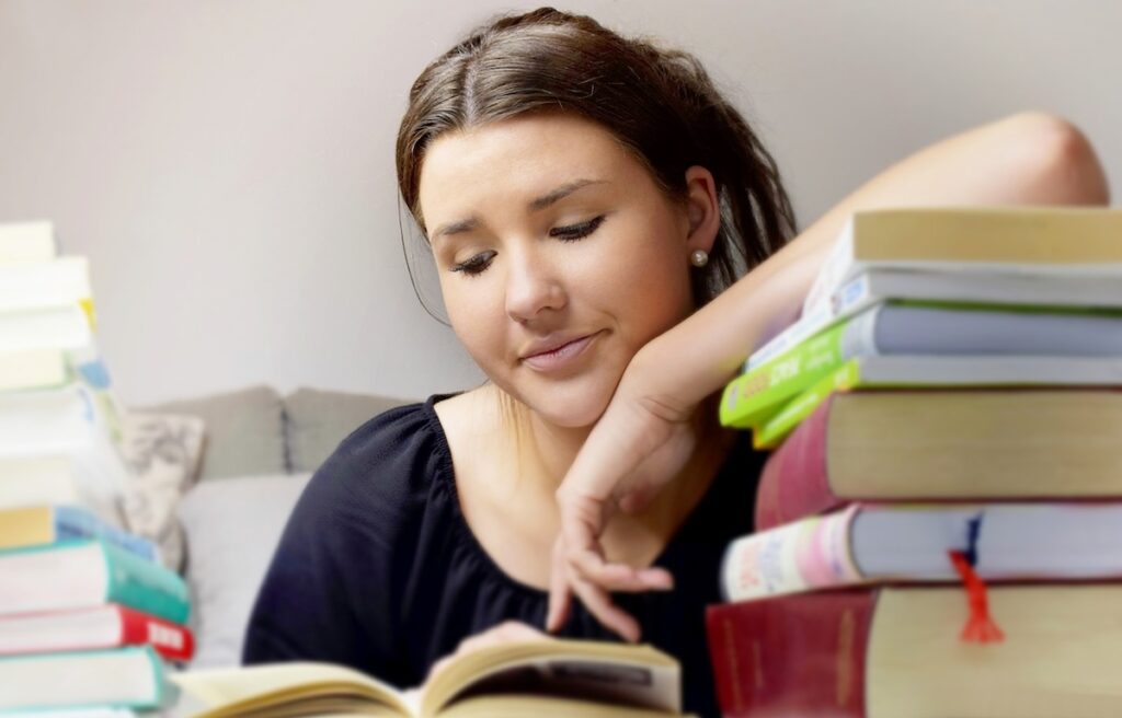 girl props her elbow on a stack of textbooks while studying her notes