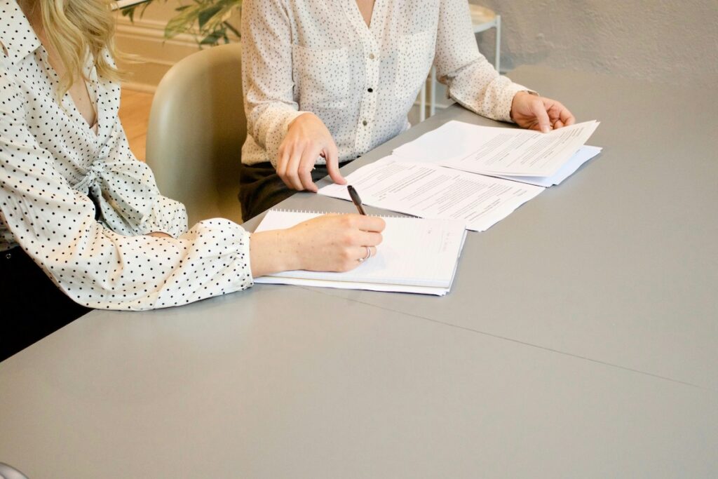 two women sit at a desk analyzing paper documents
