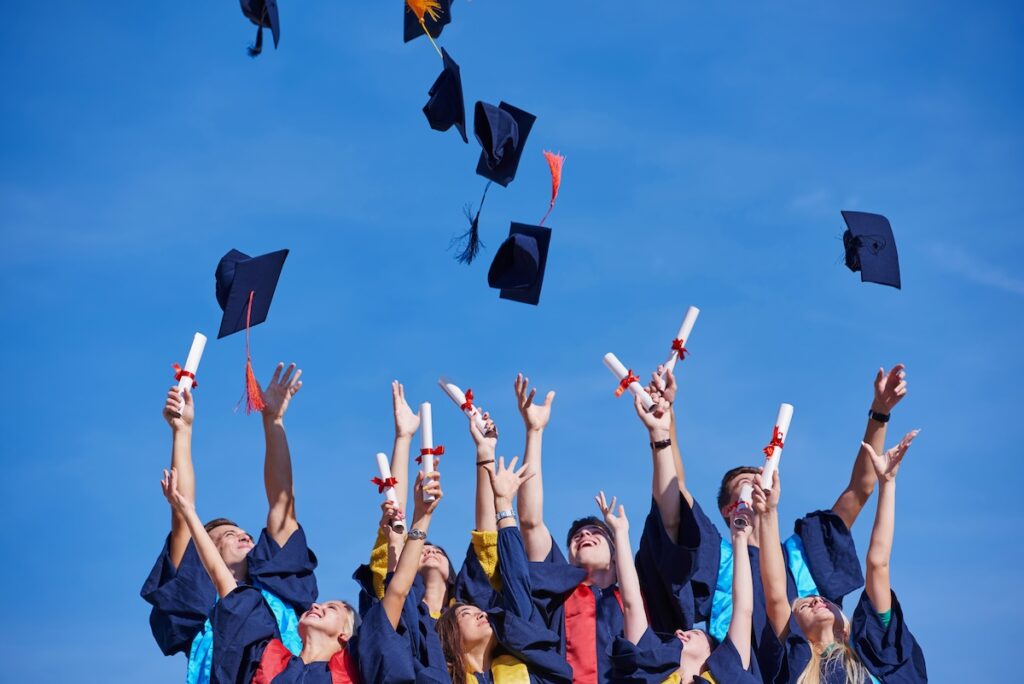 high school students graduates tossing up hats over blue sky.