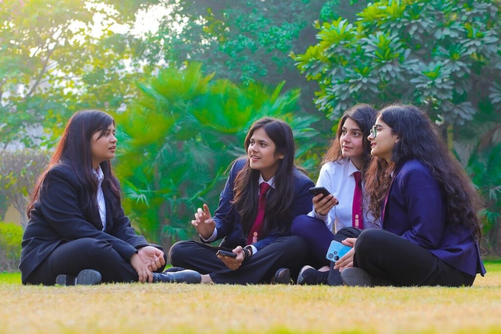 group of female students sits on grassy lawn