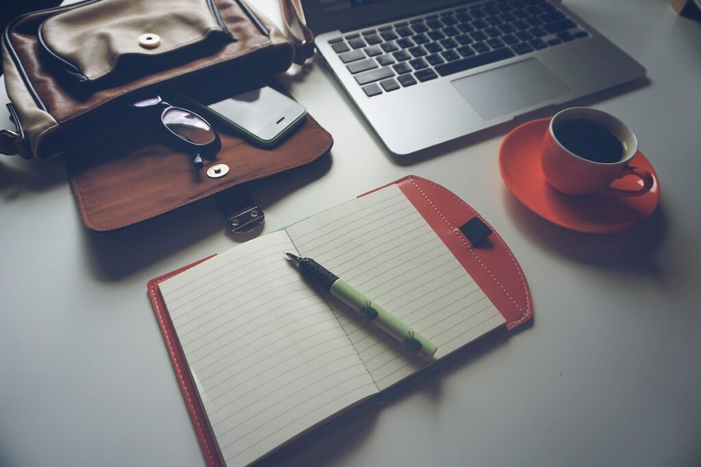 open notebook on table top next to laptop and coffee cup