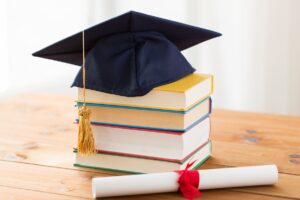 close up of books and mortarboard with diploma on wooden table